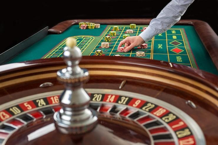 Roulette and piles of gambling chips on a green table in casino. Man hand over casino chips on roulette table